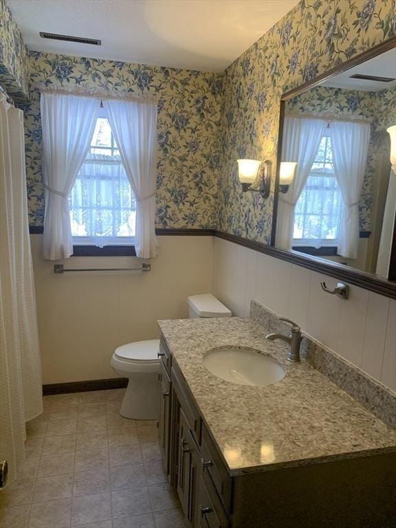 full bath featuring wainscoting, plenty of natural light, vanity, and wallpapered walls