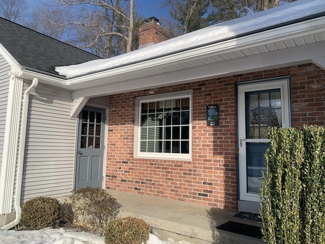 doorway to property with brick siding, a chimney, and a shingled roof