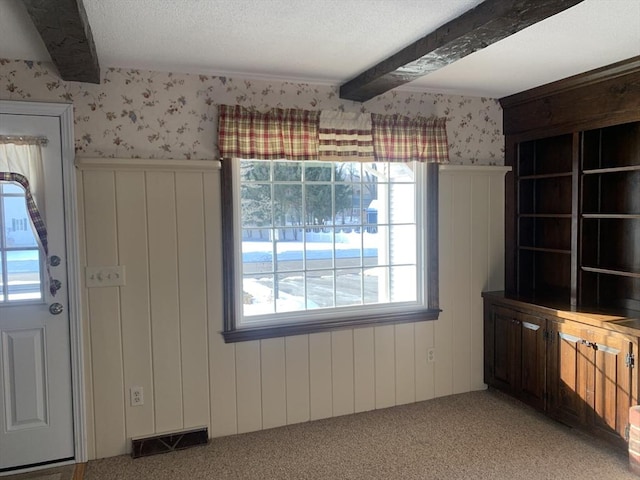 unfurnished dining area featuring visible vents, carpet flooring, beam ceiling, and wallpapered walls