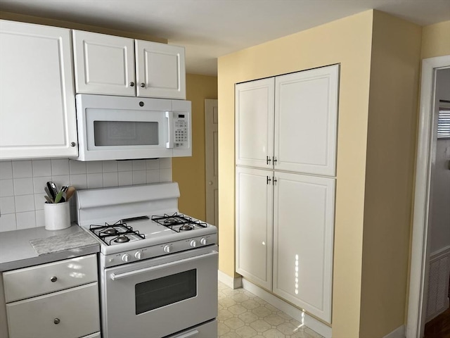 kitchen featuring white microwave, white cabinetry, range with gas stovetop, light countertops, and tasteful backsplash