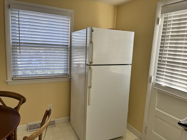 kitchen featuring light floors, freestanding refrigerator, visible vents, and baseboards