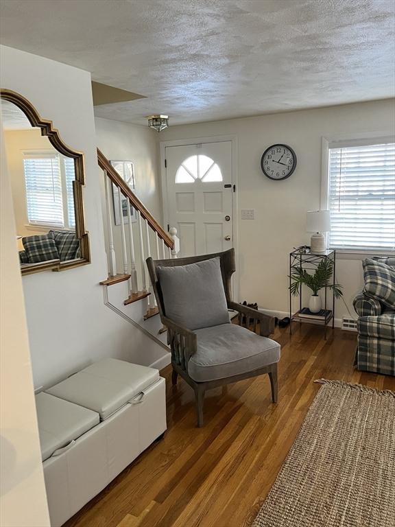 living area with a textured ceiling, stairs, baseboards, and wood finished floors