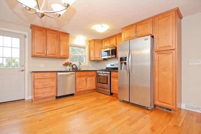 kitchen featuring visible vents, dark countertops, stainless steel appliances, light wood-type flooring, and a sink