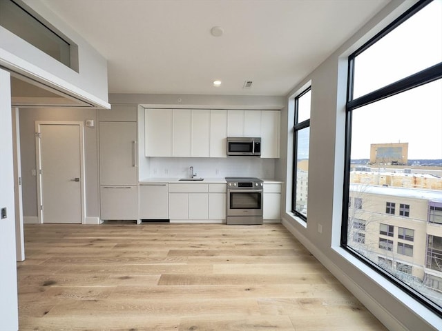 kitchen featuring white cabinetry, stainless steel appliances, a wealth of natural light, and light hardwood / wood-style flooring