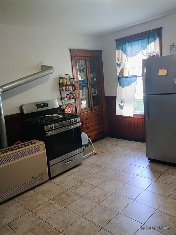 kitchen featuring stainless steel gas range oven, a wainscoted wall, freestanding refrigerator, wooden walls, and light tile patterned floors
