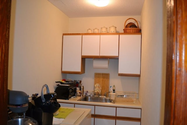 kitchen featuring white cabinets, light countertops, a textured ceiling, and a sink