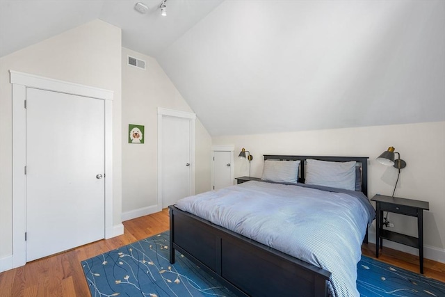bedroom with visible vents, baseboards, lofted ceiling, and wood finished floors