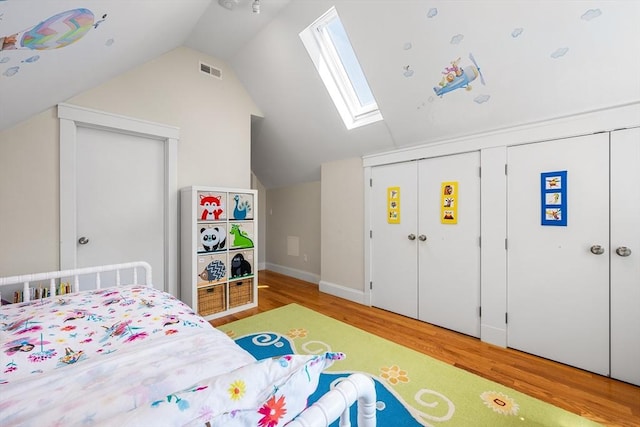 bedroom featuring vaulted ceiling with skylight, baseboards, wood finished floors, and visible vents