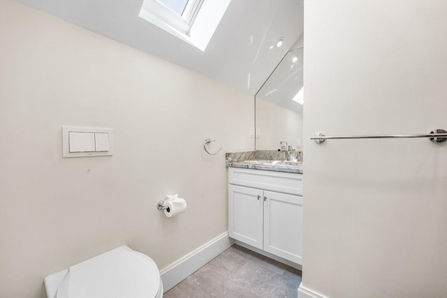 half bath featuring baseboards, toilet, a skylight, and vanity