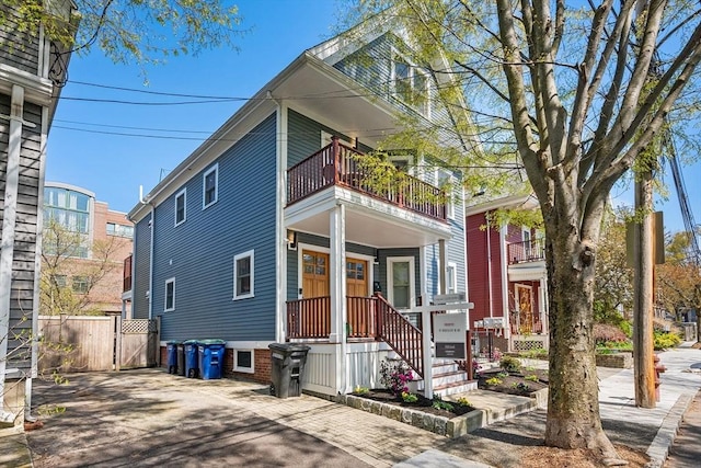 view of front facade featuring covered porch, fence, and a balcony