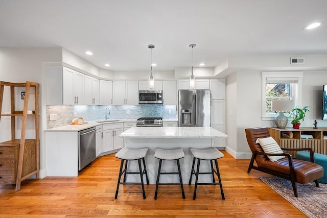 kitchen with appliances with stainless steel finishes, a sink, a center island, white cabinetry, and visible vents