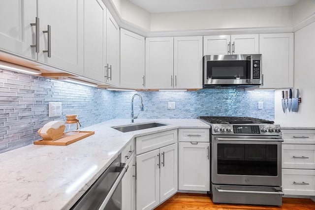 kitchen featuring light stone countertops, white cabinets, a sink, appliances with stainless steel finishes, and backsplash