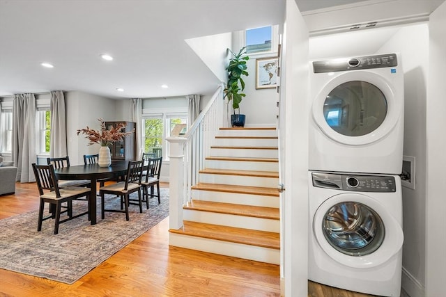 washroom with wood finished floors, recessed lighting, stacked washer / drying machine, and laundry area
