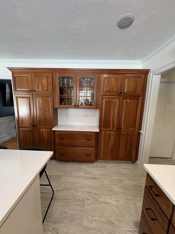 kitchen with brown cabinets, crown molding, light stone counters, and glass insert cabinets