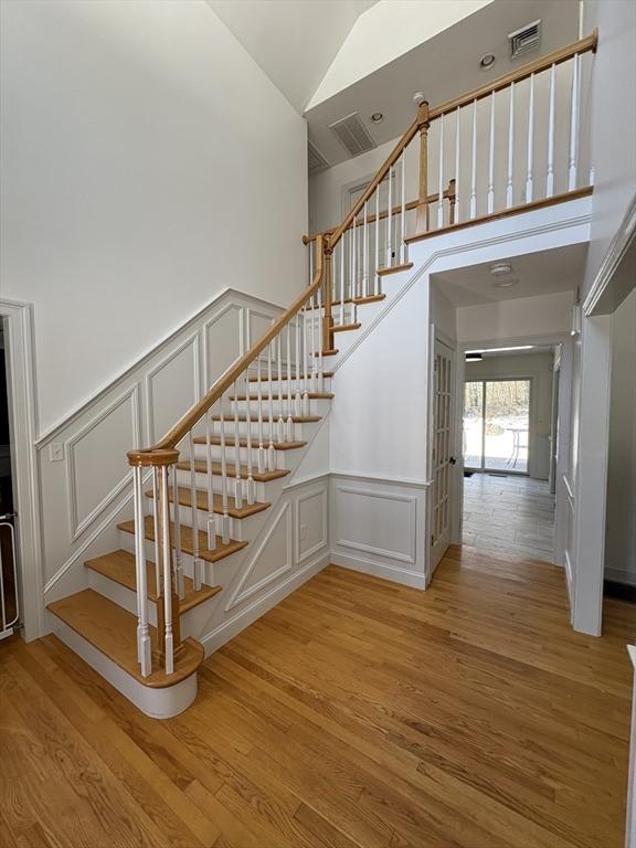 staircase with wood finished floors, visible vents, a high ceiling, and a decorative wall