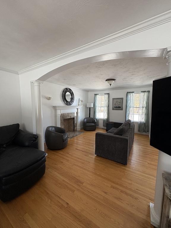 living room with crown molding, light wood-style floors, arched walkways, a fireplace, and decorative columns
