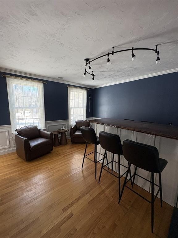 interior space featuring rail lighting, ornamental molding, a wainscoted wall, and wood finished floors