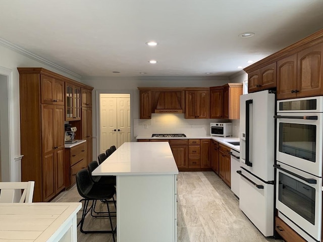 kitchen featuring white appliances, light countertops, ornamental molding, a center island, and a kitchen breakfast bar