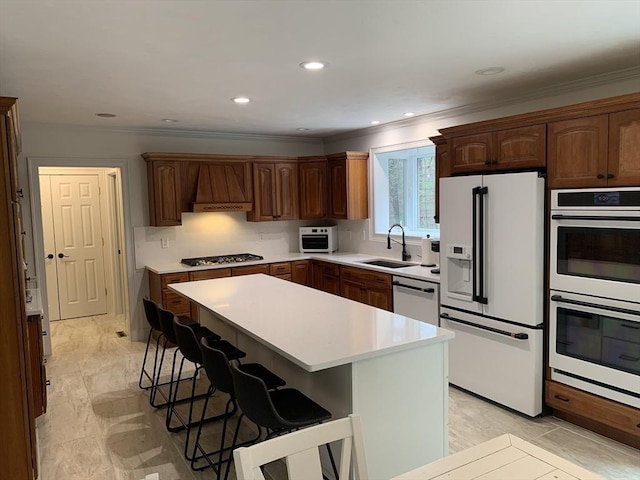 kitchen featuring a breakfast bar, custom range hood, appliances with stainless steel finishes, light countertops, and a sink