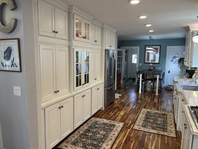 kitchen featuring decorative light fixtures, stainless steel refrigerator, dark hardwood / wood-style floors, light stone countertops, and white cabinets