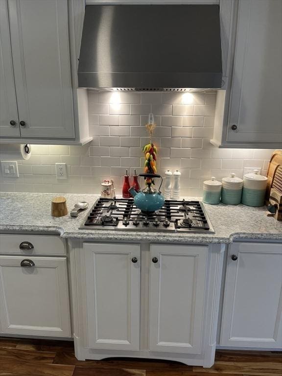 kitchen featuring tasteful backsplash, white cabinets, stainless steel gas cooktop, and wall chimney range hood