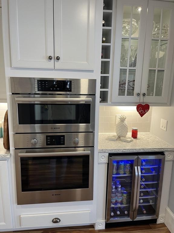 kitchen with wine cooler, white cabinets, light stone counters, and stainless steel double oven