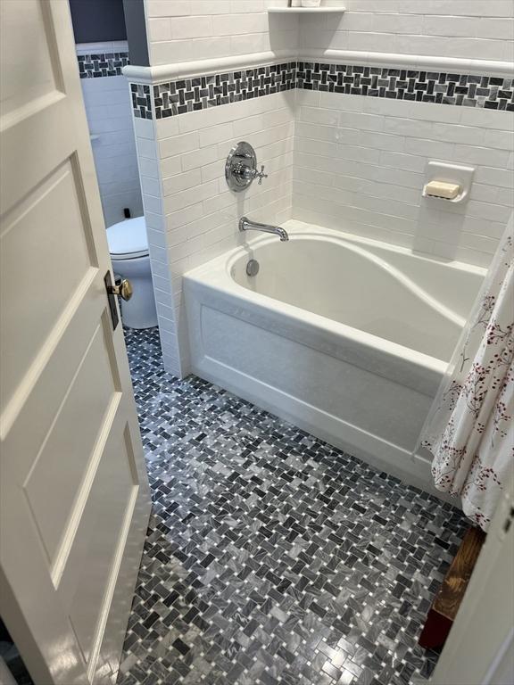 bathroom featuring tile patterned flooring, tile walls, shower / bath combination with curtain, and toilet