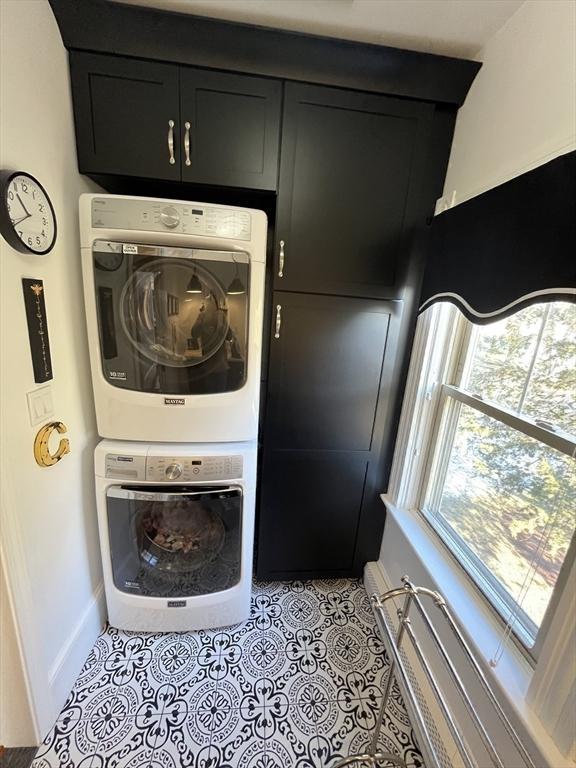 laundry area with light tile patterned flooring, stacked washer and dryer, and cabinets