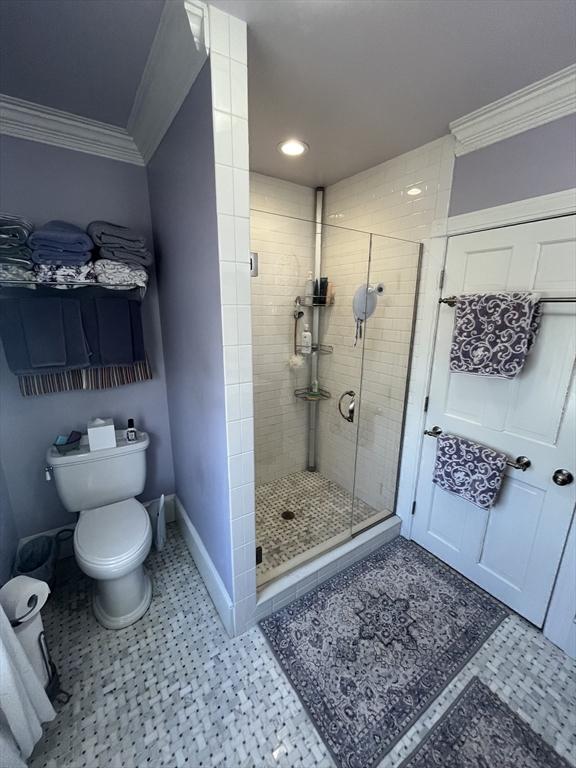 bathroom with crown molding, toilet, and a shower with shower door