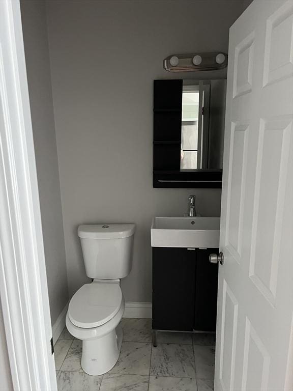half bath featuring vanity, toilet, baseboards, and marble finish floor