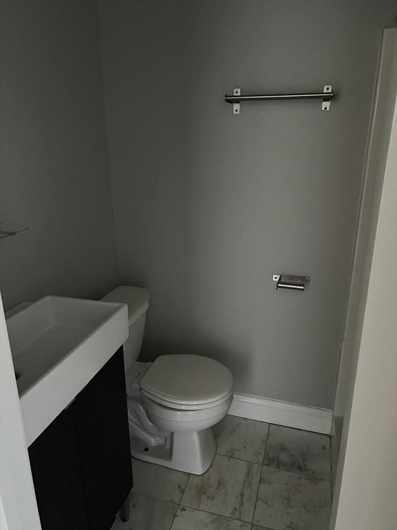 half bathroom with toilet, marble finish floor, baseboards, and vanity