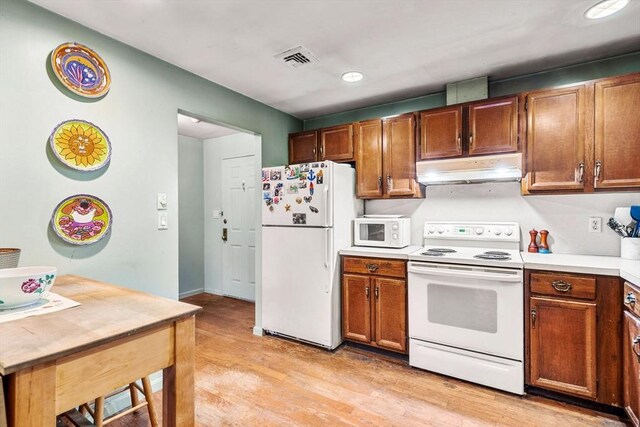 kitchen featuring white appliances, visible vents, light countertops, under cabinet range hood, and light wood-type flooring