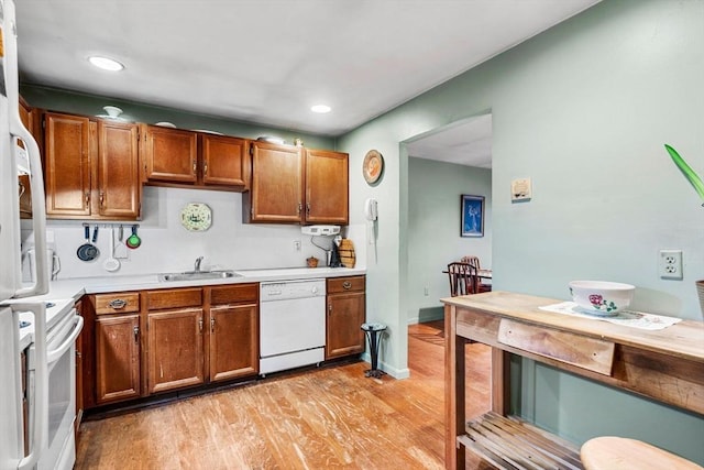 kitchen featuring light wood finished floors, light countertops, brown cabinetry, white appliances, and a sink