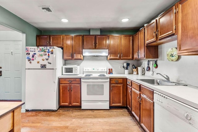 kitchen with visible vents, under cabinet range hood, a sink, white appliances, and light wood finished floors