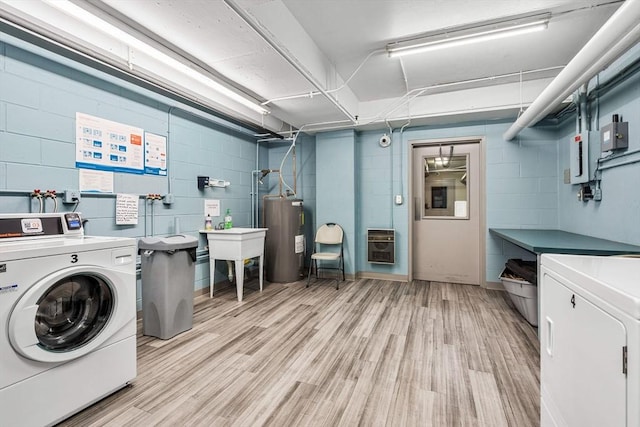 washroom with heating unit, a sink, light wood-style floors, electric water heater, and washing machine and dryer