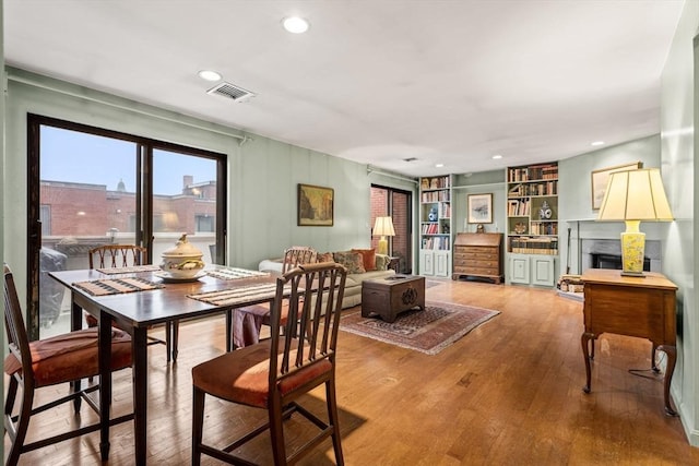 dining area featuring built in shelves, visible vents, recessed lighting, a fireplace, and hardwood / wood-style flooring