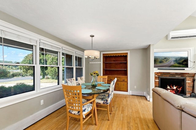 dining room featuring light hardwood / wood-style flooring, a brick fireplace, a healthy amount of sunlight, and a wall mounted AC