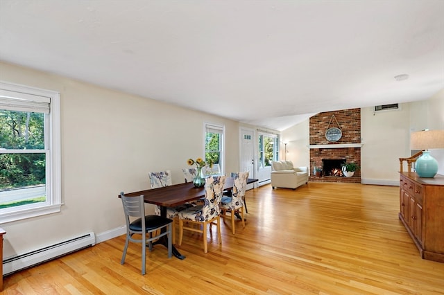 dining space with a baseboard radiator, a wealth of natural light, a brick fireplace, and light wood-type flooring