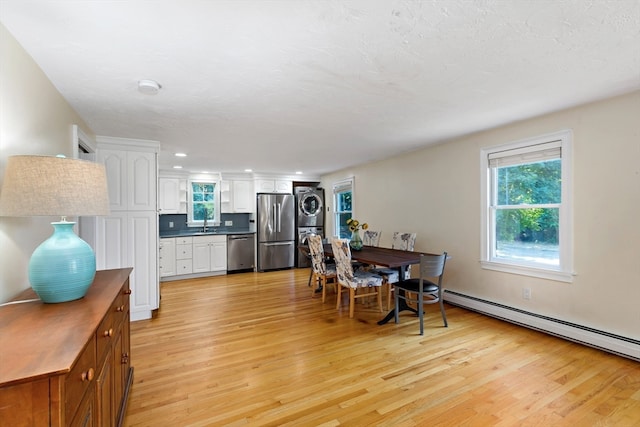 dining room featuring a baseboard heating unit, light hardwood / wood-style floors, stacked washer / drying machine, and sink