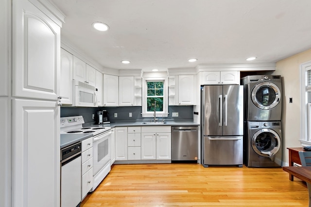 kitchen with white cabinets, sink, light hardwood / wood-style flooring, stacked washer / dryer, and appliances with stainless steel finishes