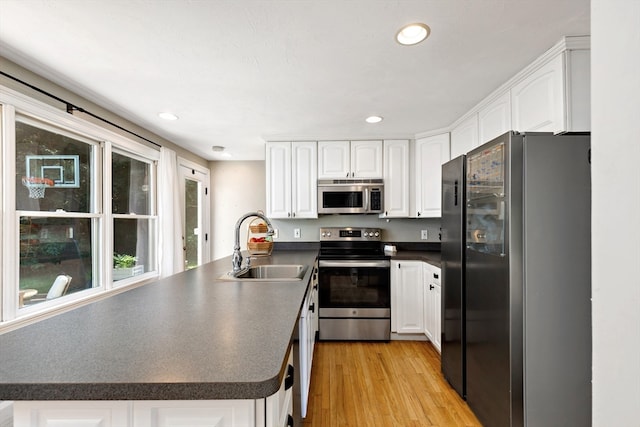 kitchen with light hardwood / wood-style floors, sink, white cabinetry, kitchen peninsula, and stainless steel appliances