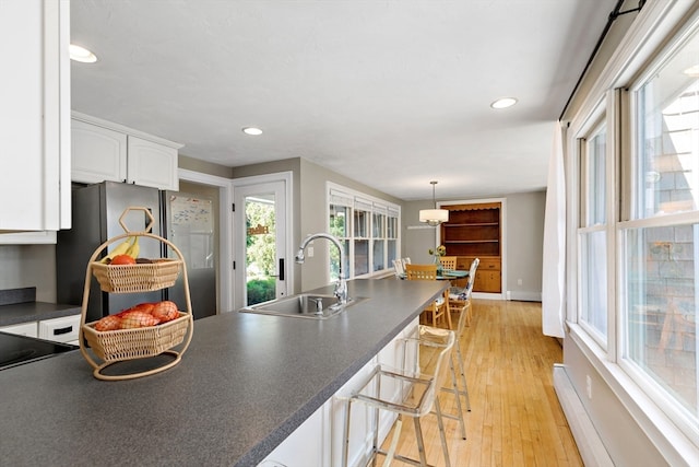 kitchen with white cabinetry, stainless steel refrigerator, pendant lighting, light hardwood / wood-style flooring, and sink