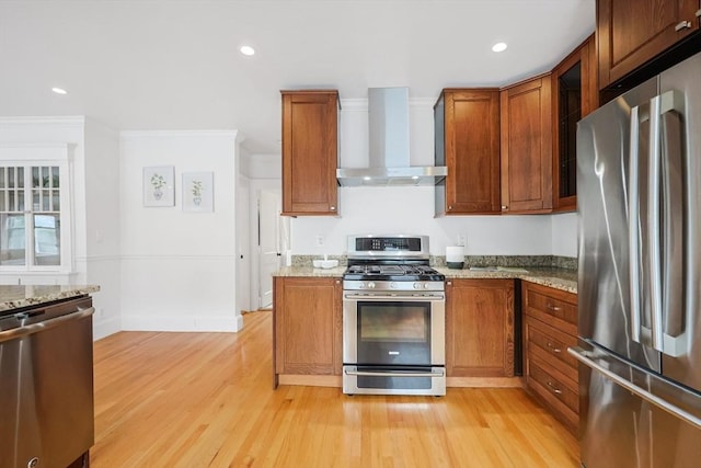 kitchen featuring stainless steel appliances, wall chimney range hood, light wood-style flooring, ornamental molding, and light stone countertops