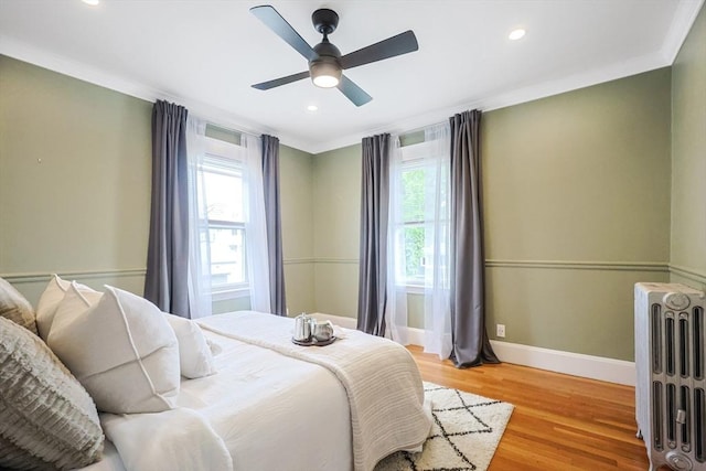 bedroom with radiator, baseboards, multiple windows, light wood finished floors, and crown molding