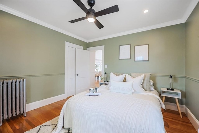 bedroom with radiator, wood finished floors, baseboards, crown molding, and a ceiling fan