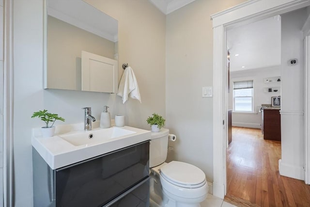 bathroom with toilet, wood finished floors, ornamental molding, vanity, and baseboards