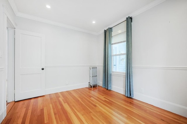 empty room featuring radiator heating unit, light wood-style flooring, crown molding, baseboards, and recessed lighting