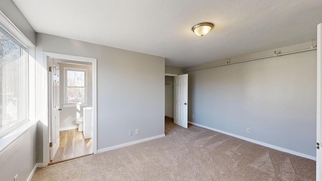 unfurnished bedroom featuring connected bathroom, light colored carpet, and multiple windows