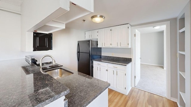 kitchen featuring white cabinets, kitchen peninsula, black fridge, and light hardwood / wood-style floors