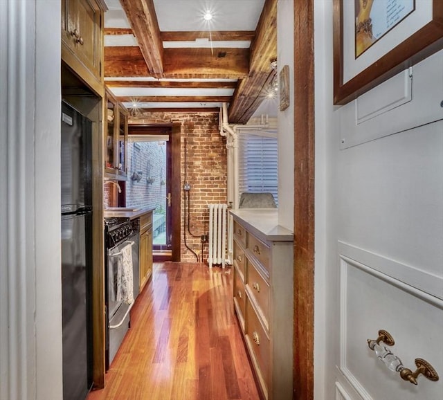 kitchen with light wood-type flooring, gas range, sink, beam ceiling, and radiator heating unit